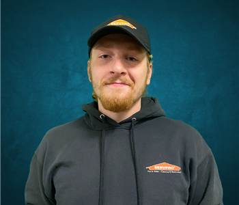 Male employee with red hair smiling in front of a blue background. 