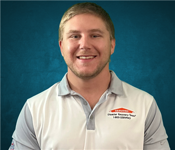 Male employee with blonde hair smiling in front of a blue background. 