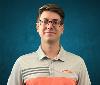 Male employee with brown hair smiling in front of a blue background. 