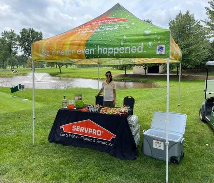 a woman standing behind a SERVPRO table with a tent overhead