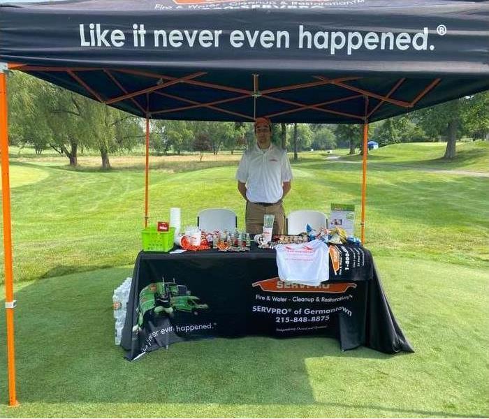 Young man standing behind a table full of giveaways and a SERVPRO tent overhead