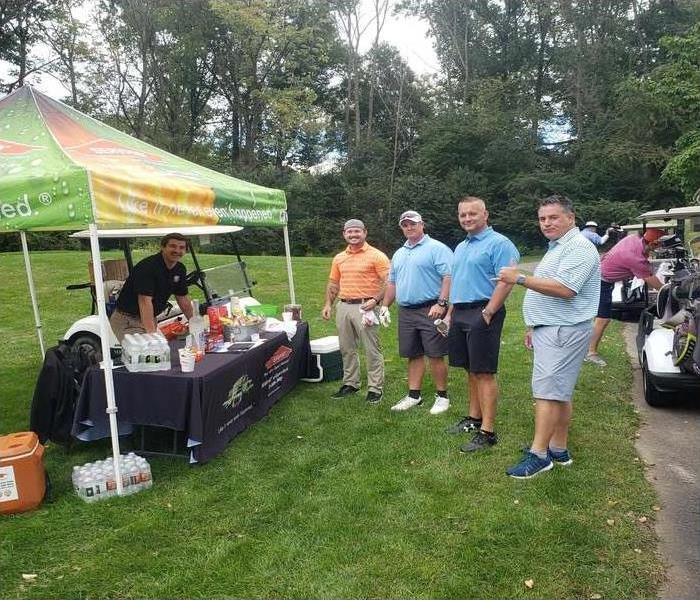 4 male golfers posing for a photo in front of a man in a SERVPRO tent