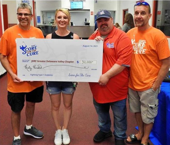 4 people standing in a row holding an oversized check