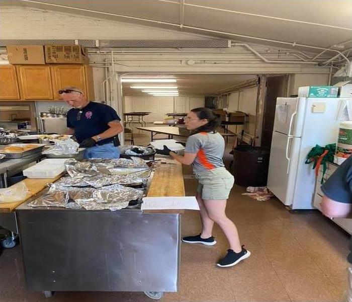 a man and women in a kitchen grabbing foil containers