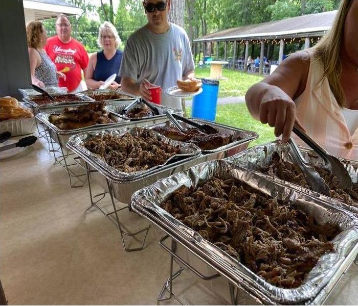 people serving themselves from a table with different meats in trays